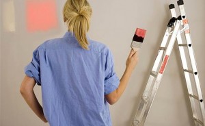 Woman decorating at home, painting wall, holding paintbrush dipped in red paint, rear view